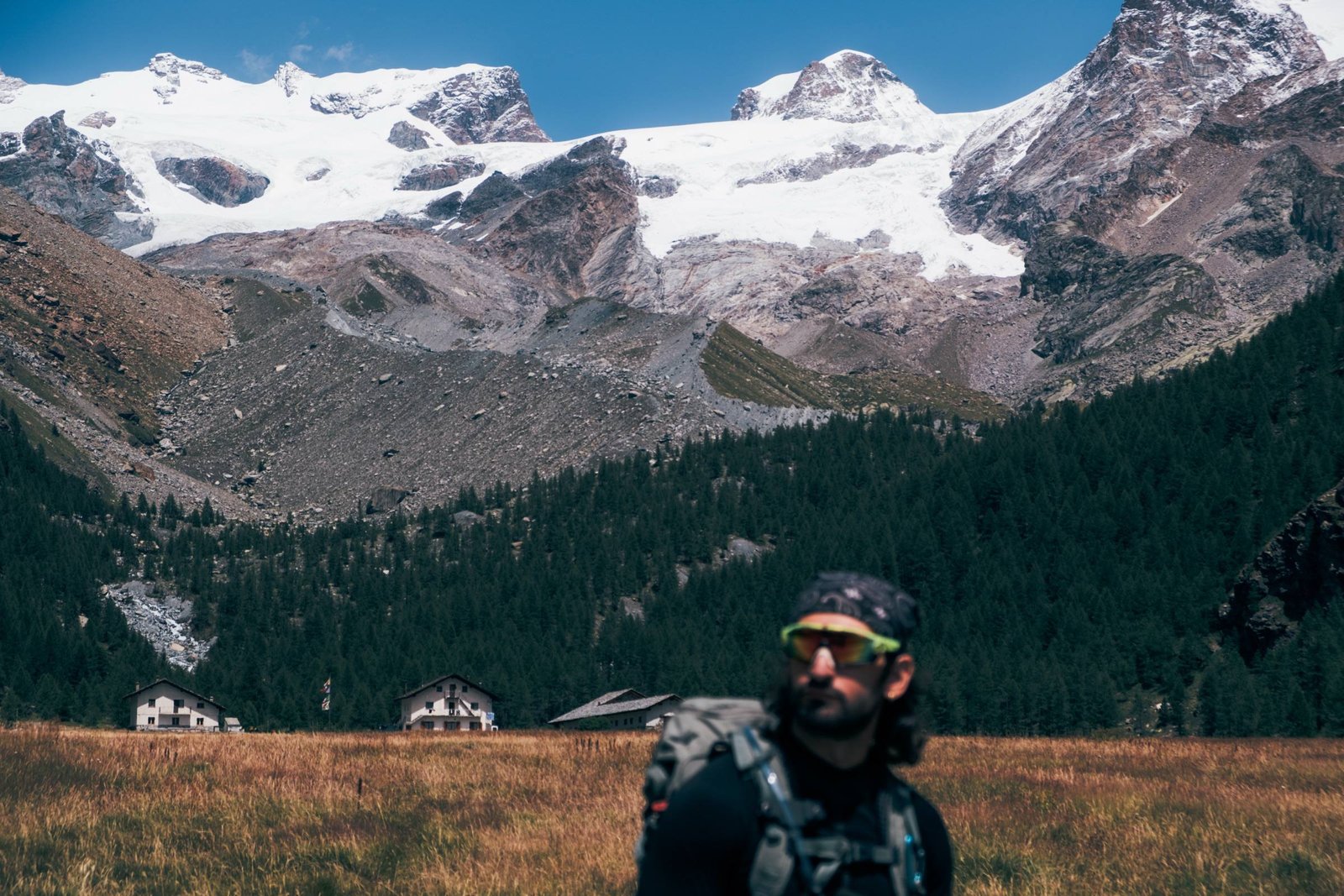Esploratore con zaino in una valle alpina davanti ai ghiacciai