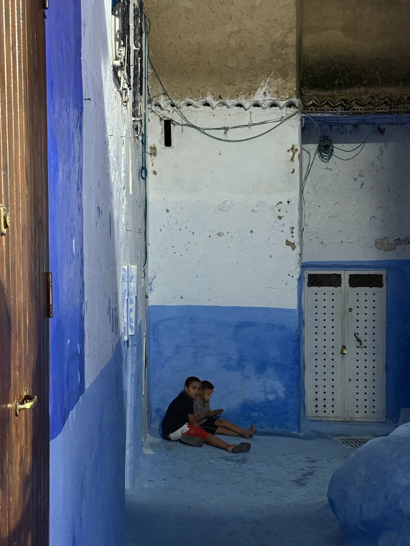 Un bambino seduto vicino a una porta blu in un vicolo di Chefchaouen