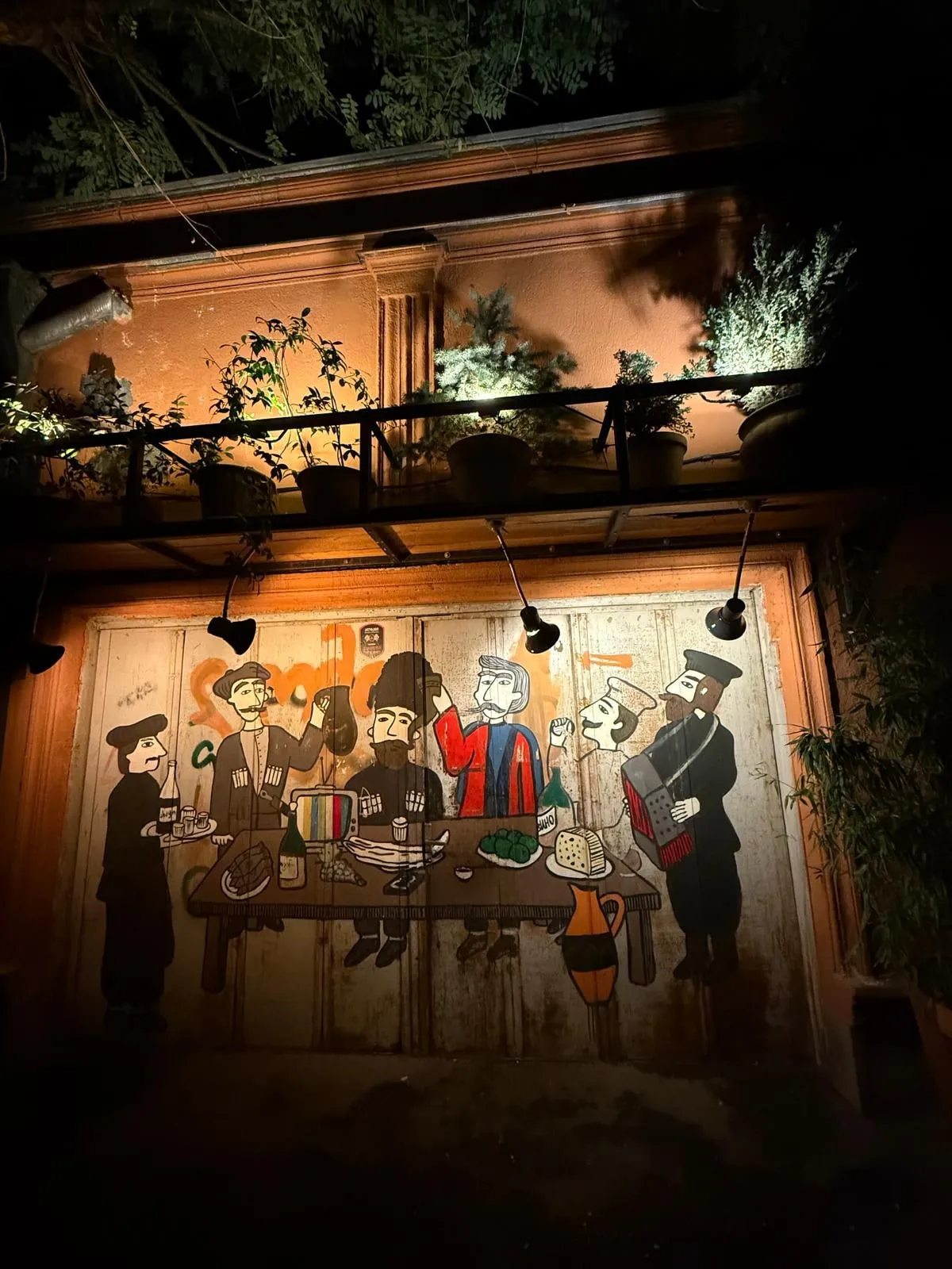 Un murale con una tavolata dipinto su una porta, illuminato di sera